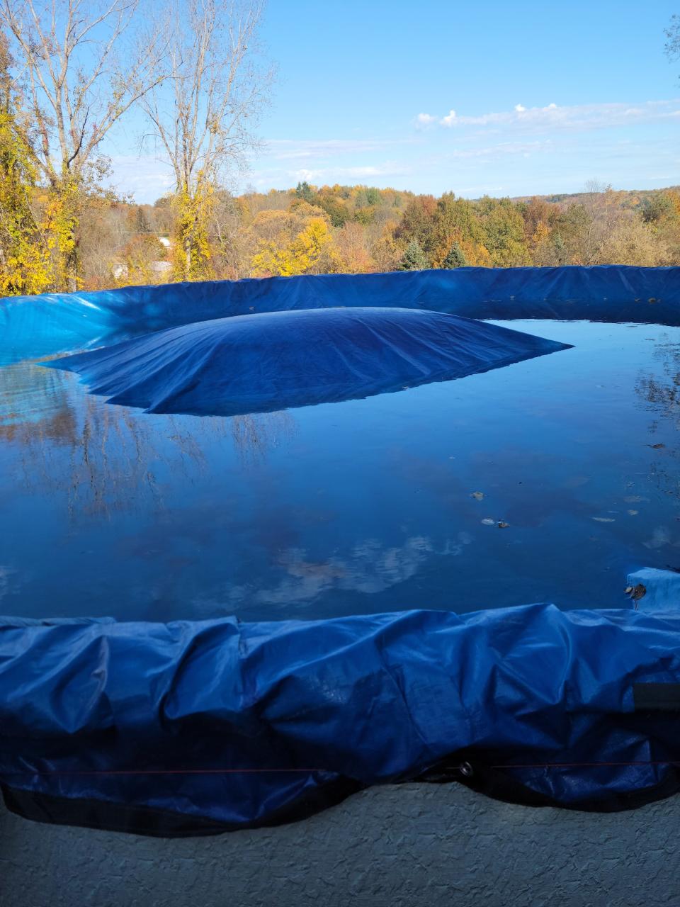 A round pool closed for the winter with pool pillow rising from beneath the cover. 