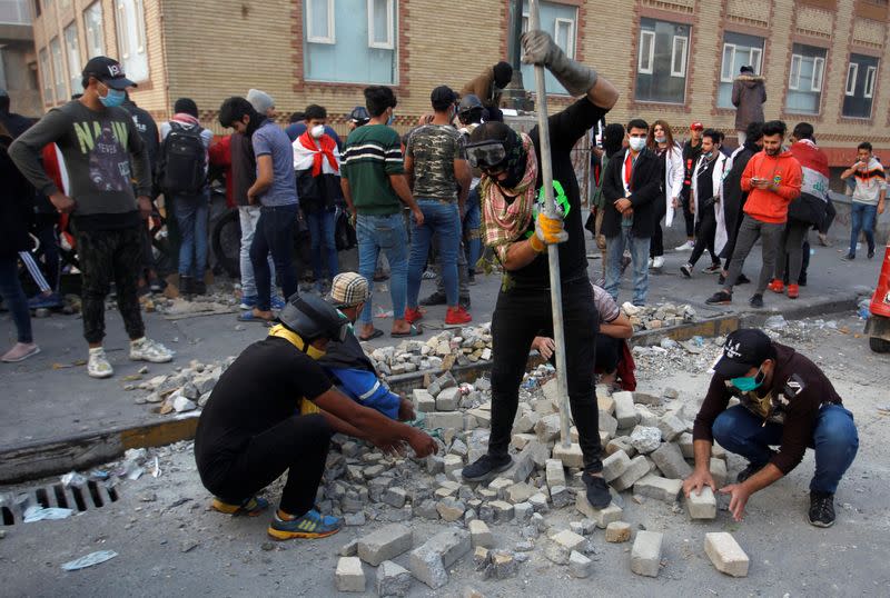 Iraqi demonstrators smash stones to throw them toward Iraqi security forces during the ongoing anti-government protests, in Baghdad