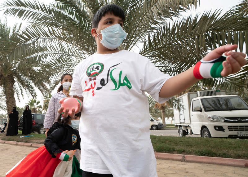 A Kuwaiti boy wears a protective face mask, following the outbreak of the new coronavirus, as he throws water at passing cars, during celebrations for the 29th Kuwait Liberation Day from the Iraqi occupation, in Kuwait City