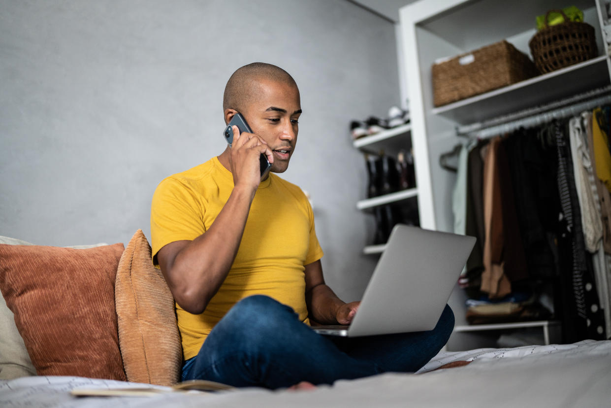 Young man talking on the mobile phone and using the laptop at home