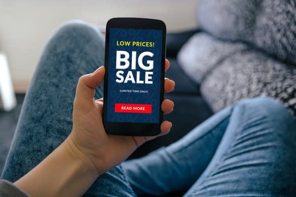 A person holding a cell phone that reads Low Prices Big Sale limited time only read more.