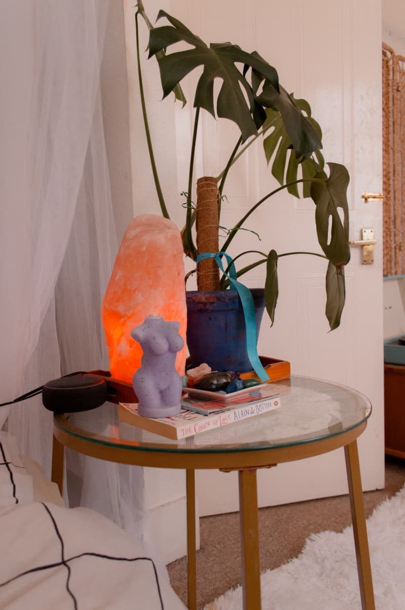 A nightstand with candles, plants, and a glowing rock lamp.
