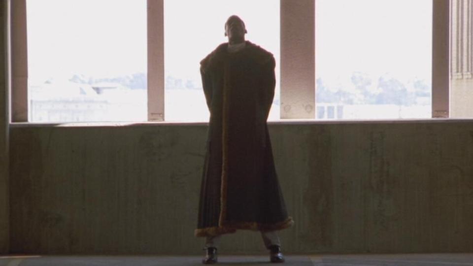 Tony Todd as Candyman stands in a parking garage wearing a long brown fur coat