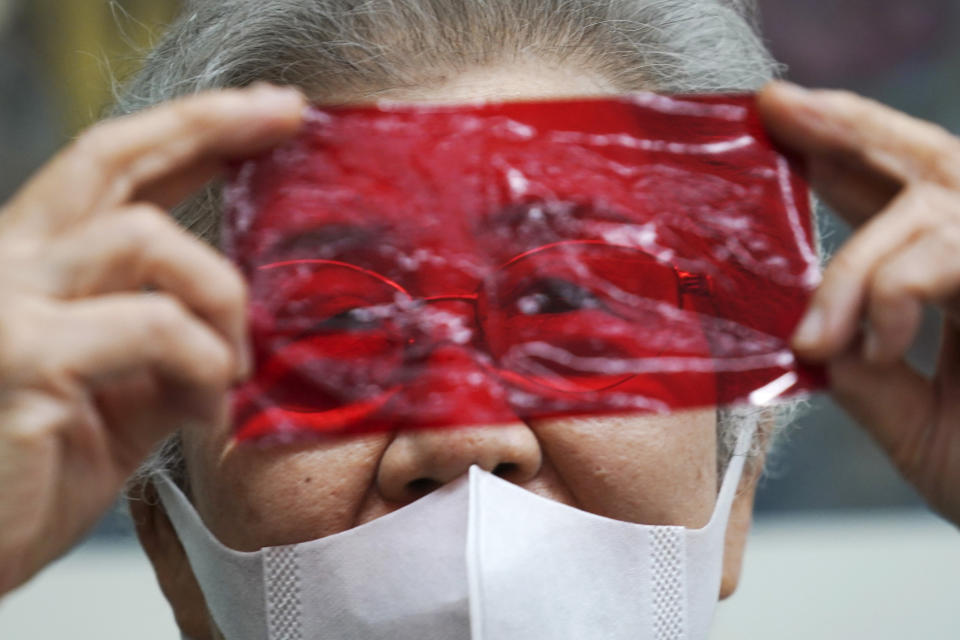 Kisako Motoki, 86, speaks, looking though a red cellophane depicting what she saw the atmosphere of the night of the Great Tokyo Air Raid on March 10, 1945, during an interview with the Associated Press at the Center for the Tokyo Raids and War Damage in Tokyo Wednesday, July 29, 2020. In Japan, war orphans were punished for surviving. They were bullied. They were called trash, sometimes rounded up by police and put in cages. Some were sent to institutions or sold for labor. They were targets of abuse and discrimination. Now, 75 years after the war's end, some are revealing their untold stories of recovery and pain, underscoring Japan’s failure to help its own people. (AP Photo/Eugene Hoshiko)