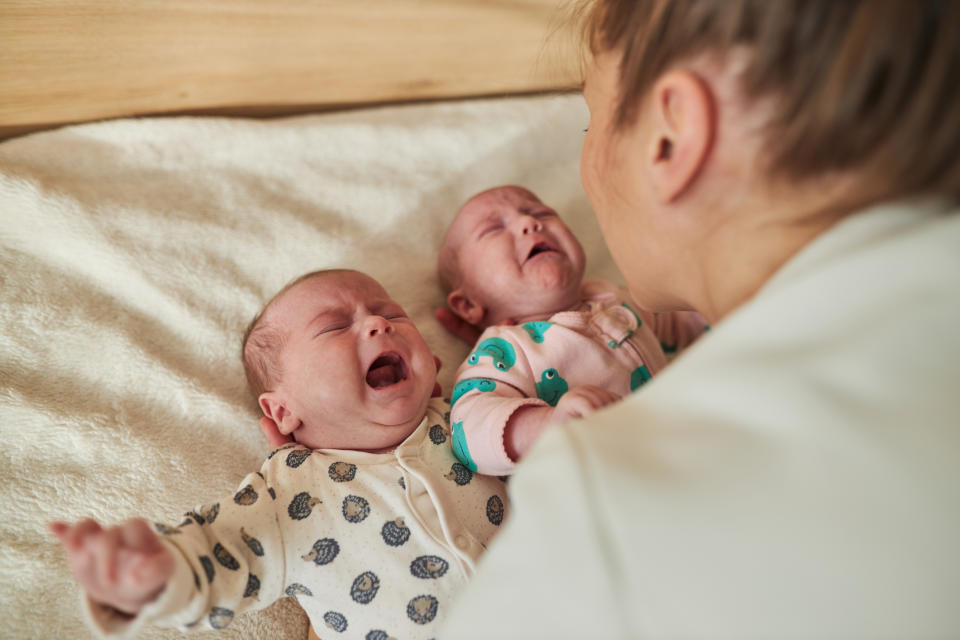 Mom looking at crying newborn twins lying on a soft surface