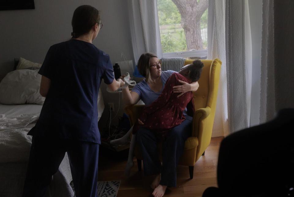 Jessie Sage Cheng receives a towel from a nurse to help wipe the face of her 11-year-old daughter at their home in Duncanville, TX on April 9, 2024. Cheng has a nurse to help her care for her daughter as she balances working as a nurse herself, going to grad school, and being a single mother.