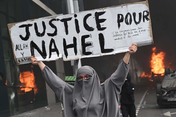 PHOTO: A protester holds a banner reading 'Justice for Nahel' as cars burn in the street in the Paris suburb of Nanterre, France, on June 29, 2023, at the end of a commemoration march for a 17-year-old driver who was shot dead by a police officer. (Bertrand Guay/ AFP via Getty Images)