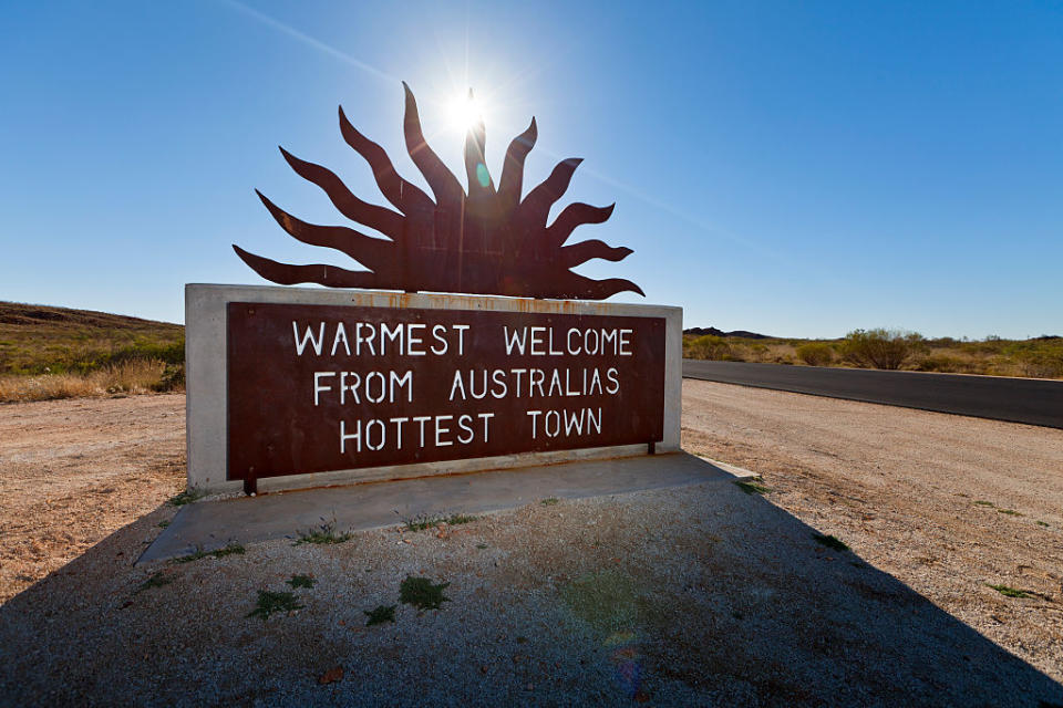 Sign reading "Warmest welcome from Australia's hottest town" with a sun design, placed outdoors