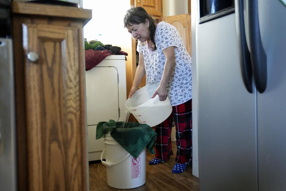 Celia Magdaleno strains boiled water before giving her husband a bath following an earthquake in Rio Dell, Calif., Wednesday, Dec. 21, 2022. Magdaleno's husband is undergoing dialysis treatment and said is crucial for him to be clean before receiving treatment to avoid infections. (AP Photo/Godofredo A. Vásquez)