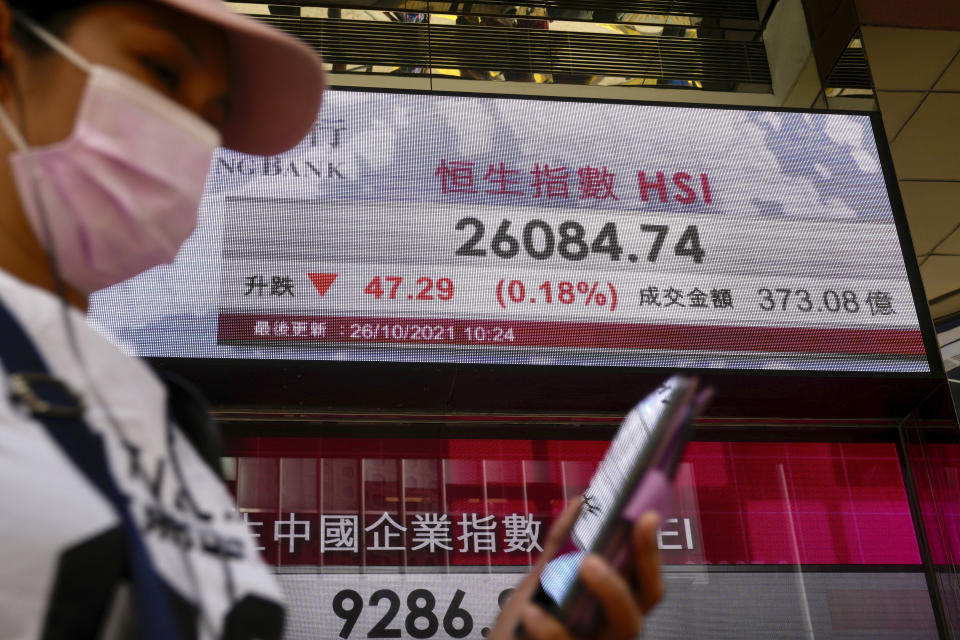 A woman wearing a face mask walks past a bank's electronic board showing the Hong Kong share index in Hong Kong, Tuesday, Oct. 26, 2021. Asian shares were mostly higher Tuesday after another rally to a record high on Wall Street. (AP Photo/Kin Cheung)