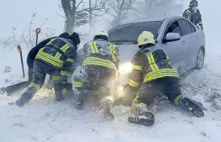 En esta foto proporcionada por el Servicio de Emergencia de Ucrania, trabajadores de emergencia ucranianos intentan empujar un automóvil atrapado en la nieve en la autopista de la región de Odesa, Ucrania, el lunes 27 de noviembre de 2023. 