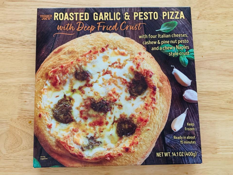 dark-colored box of Trader Joe's roasted garlic and pesto pizza on wood table