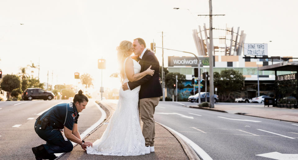 A photo of the couple kissing while the paramedic holds the bride's dress in place.