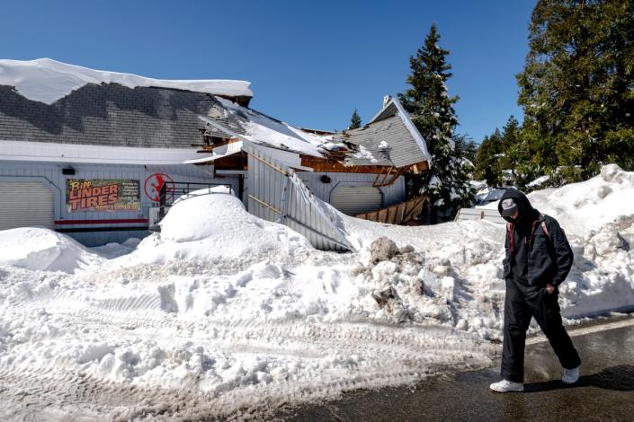 A man walks past a damaged tire shop in Crestline, Calif., Friday, March 3, 2023, following a huge snowfall that buried homes and businesses. (Watchara Phomicinda/The Orange County Register via AP) (© The Riverside Press-Enterprise)