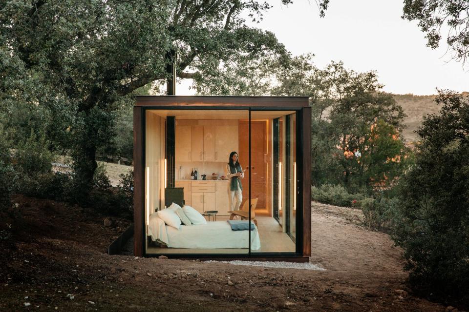 The Tini M bedroom is surrounded by windows. The initial structure includes a bed base with drawers, bedside tables, and a wood stove.