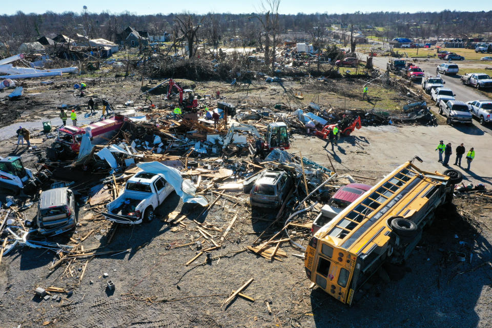 Searchers look for victims in the wreckage from a tornado in Mayfield, Kentucky. A school bus lying on its side and other damaged vehicles can be seen among the debris.