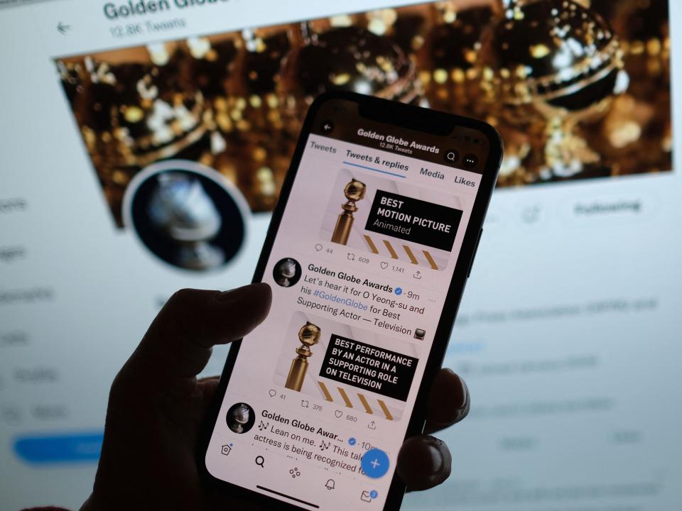 Someone holding an iPhone with the Golden Globes Twitter account open in front of a computer screen with the Golden Globes Twitter account open.