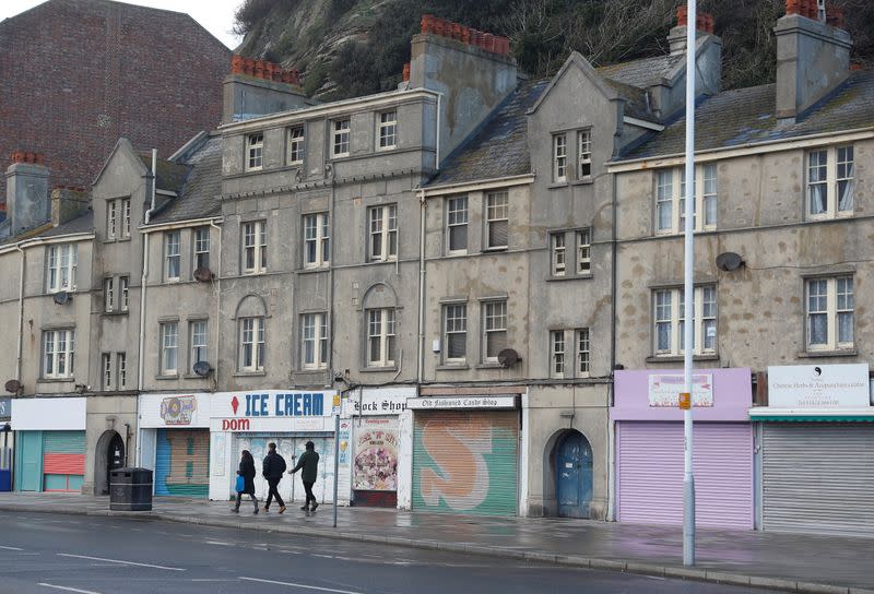 People walk past shuttered shops on the seafront as the British government imposes stricter tiers of restrictions amid the coronavirus disease (COVID-19) pandemic, in Hastings