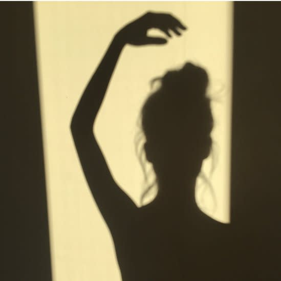 Shadow of a ballerina standing in a doorway with her hand above her head.