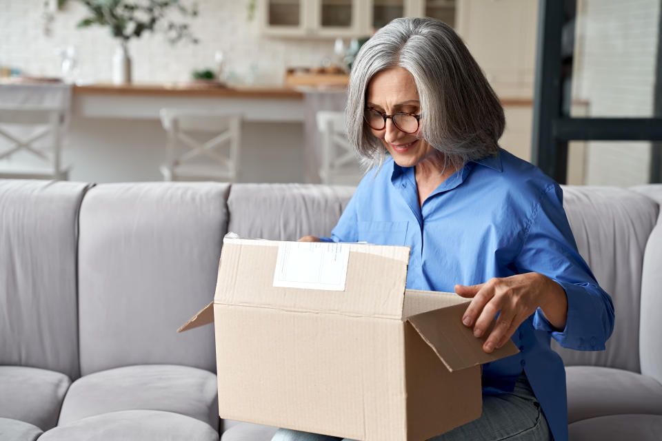 Smiling mature woman customer unpacking parcel from Temu order.