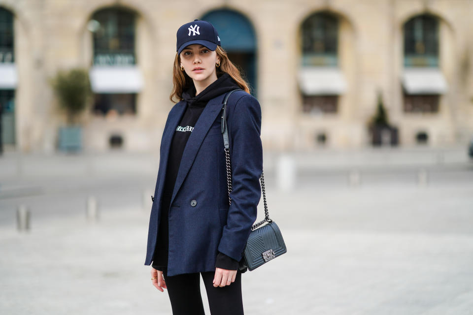 PARIS, FRANCE - MARCH 03: Olesya Senchenko wears a NY blue cap hat, a black hoodie sweater, a navy blue blazer jacket, a black leather quilted Chanel bag, black leggings, on March 03, 2021 in Paris, France. (Photo by Edward Berthelot/Getty Images)