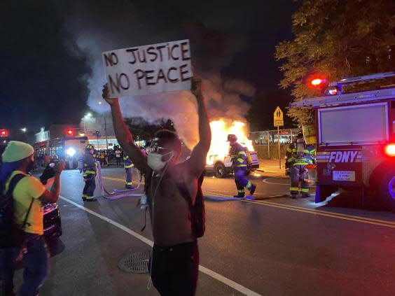 A protester stands in front of a burning police car in Brooklyn on Saturday, May 30. (Richard Hall / The Independent)