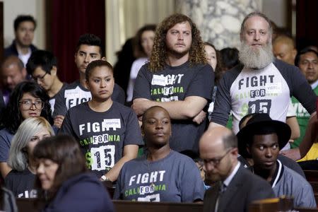 People stand as the Los Angeles City Council prepares to vote on a proposal to raise the minimum wage to $15.00 per hour in Los Angeles, California June 3, 2015. REUTERS/Jonathan Alcorn