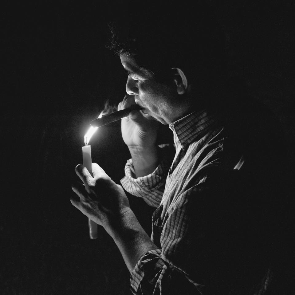 <p>Diego Gonzalez, shaman and healer, lights a cigar to be used as a ritual offering. (Photograph by Fran Antmann) </p>