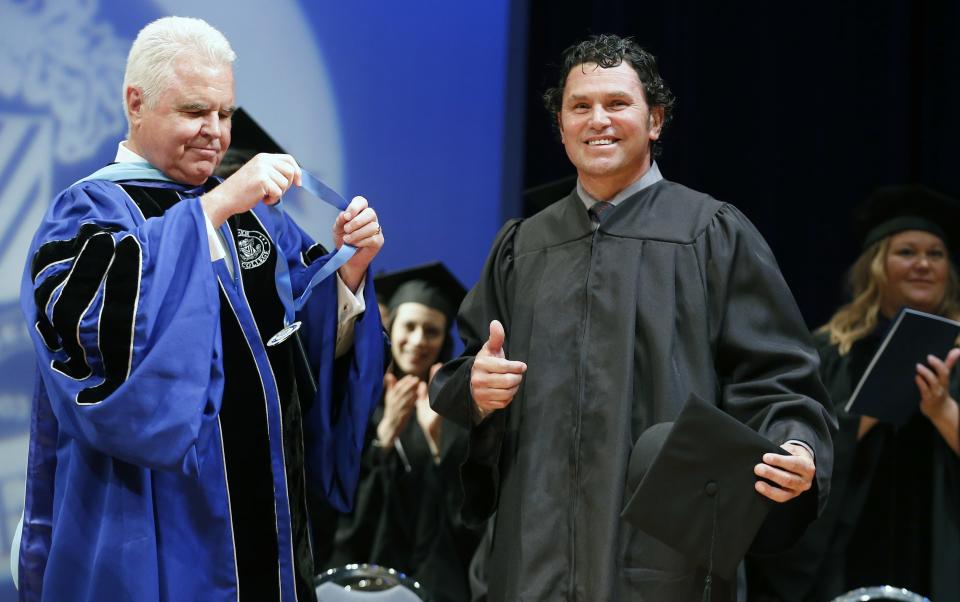 Boston Marathon bombing specttor Carlos Arredondo reacts after receiving an honorary degree from the president of Fisher College Dr. Thomas McGovern, left, during commencement ceremonies in Boston, Saturday, May 10, 2014. Arredondo and bombing survivor Jeff Bauman, who'se life Arredondo saved the day of the bombing, each gave graduation speeches and were awarded honorary degrees. (AP Photo/Michael Dwyer)