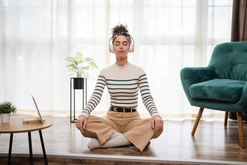 one woman adult caucasian female millennial using headphones for online guided meditation practicing mindfulness yoga with eyes closed on the floor at home real people self care concept copy space