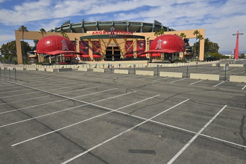 A parking lot is empty as people walk by the front of Angel Stadium, Thursday, June 25, 2020, in Anaheim, Calif. By the time Major League Baseball returns in late July, it will have been more than four months since teams last played. The season is now going to be a 60-game sprint to the finish, held in ballparks without fans and featuring some unusual rules. (AP Photo/Mark J. Terrill)