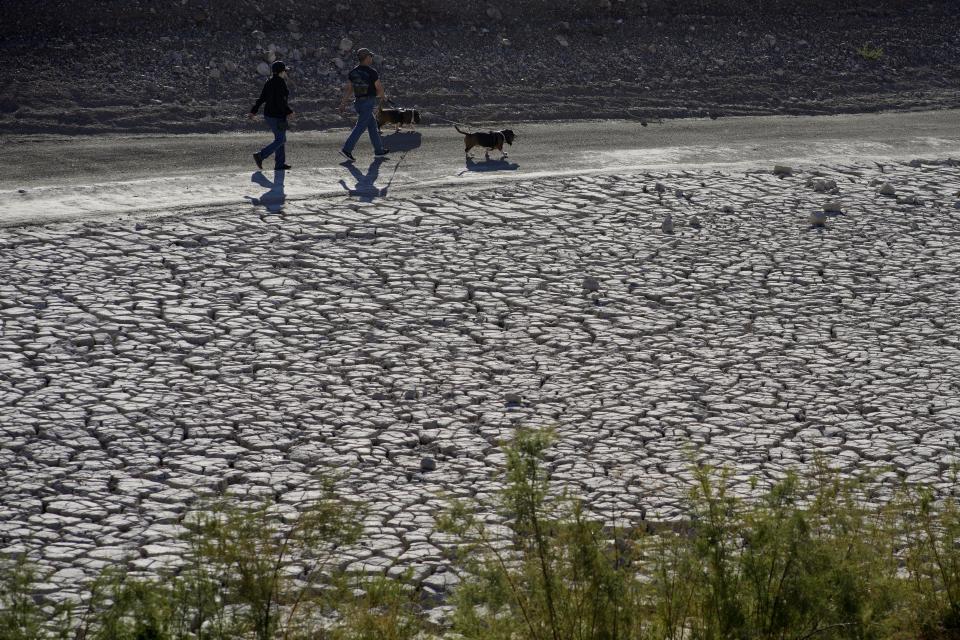 FILE - People walk by cracked earth in an area once under the water of Lake Mead at the Lake Mead National Recreation Area, Jan. 27, 2023, near Boulder City, Nev. More Americans believe they've personally felt the impact of climate change because of recent extreme weather according to new polling from The Associated Press-NORC Center for Public Affairs Research. (AP Photo/John Locher, File)