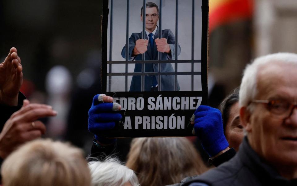 A demonstrator holds up a placard with a picture of Pedro Sanchez in jail and reading "Pedro Sanchez to jail" and "For seven votes you have your ass broken" during a protest against the Spanish prime minister and his government, near the Spanish Socialist Workers' Party headquarters in Madrid, on Friday