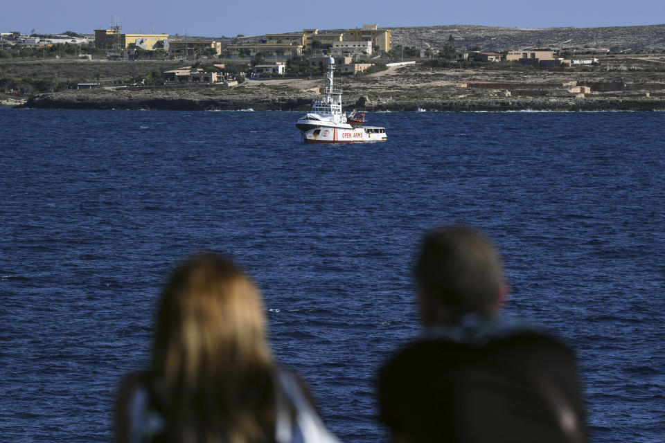 People on a ferry boat look at the Open Arms vessel, with 107 migrants on board, anchored off the Sicilian vacation and fishing island of Lampedusa, southern Italy, Monday, Aug. 19, 2019. Open Arms on Monday suggested chartering a plane to fly to Spain the migrants blocked off the coast of Italy aboard its boat since early August, to end a stalemate with the Italian Interior minister Matteo Salvini, who won't let private rescue boats into his nation's ports. (AP Photo/Salvatore Cavalli)