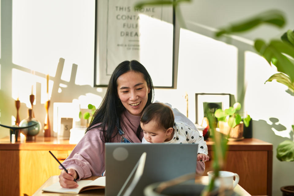 Mature small business owner sitting at table with child on lap and making notes, multitasking, working mother, efficiency