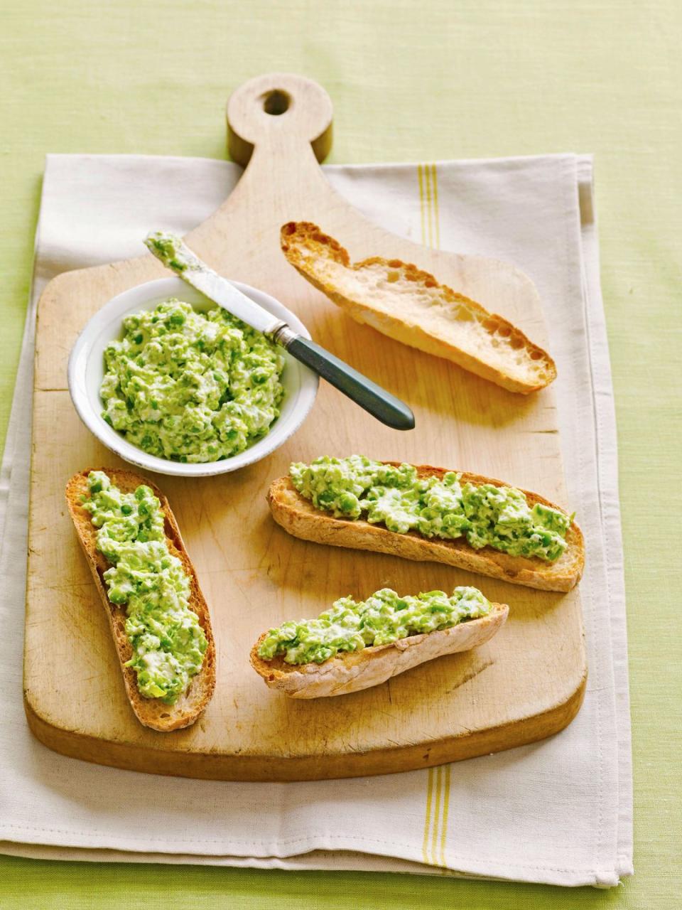 ricotta pea spread in a white bowl with sliced crusty bread on a wooden serving board