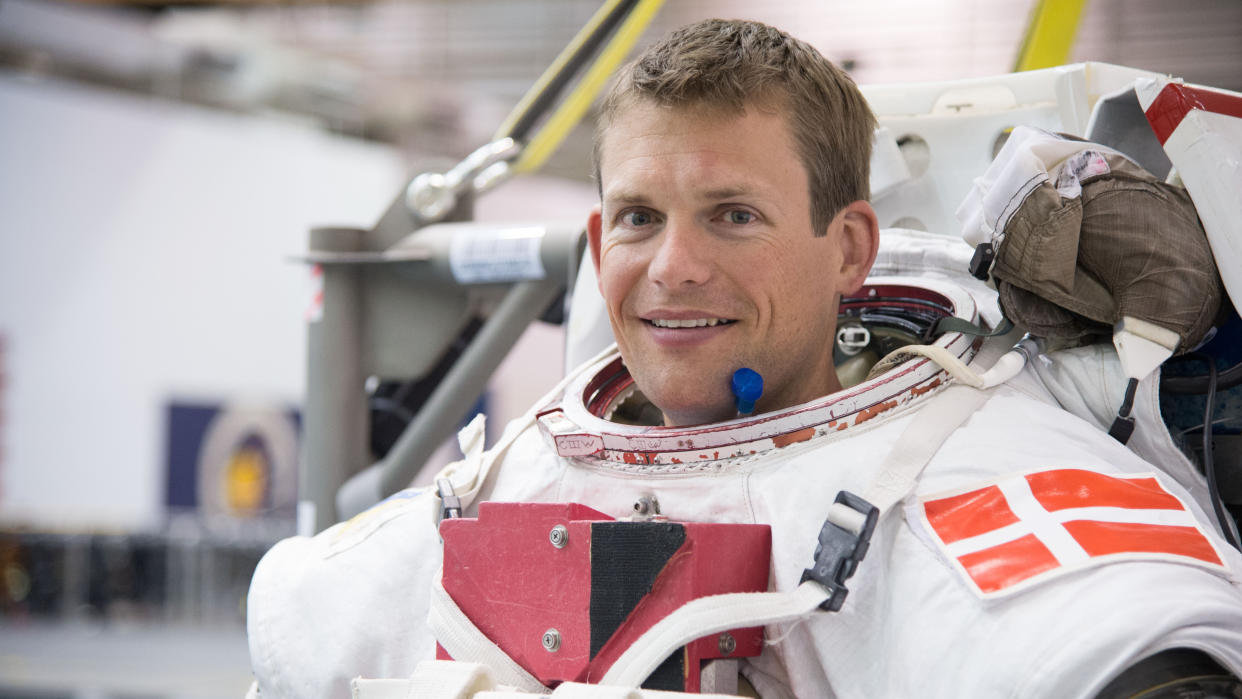 Andreas mogensen visible in a spacesuit from the shoulders up, inside a large facility. 