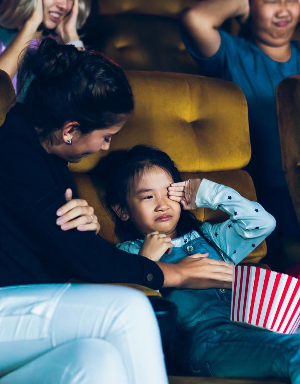 child crying while parent comforts them in movie theater