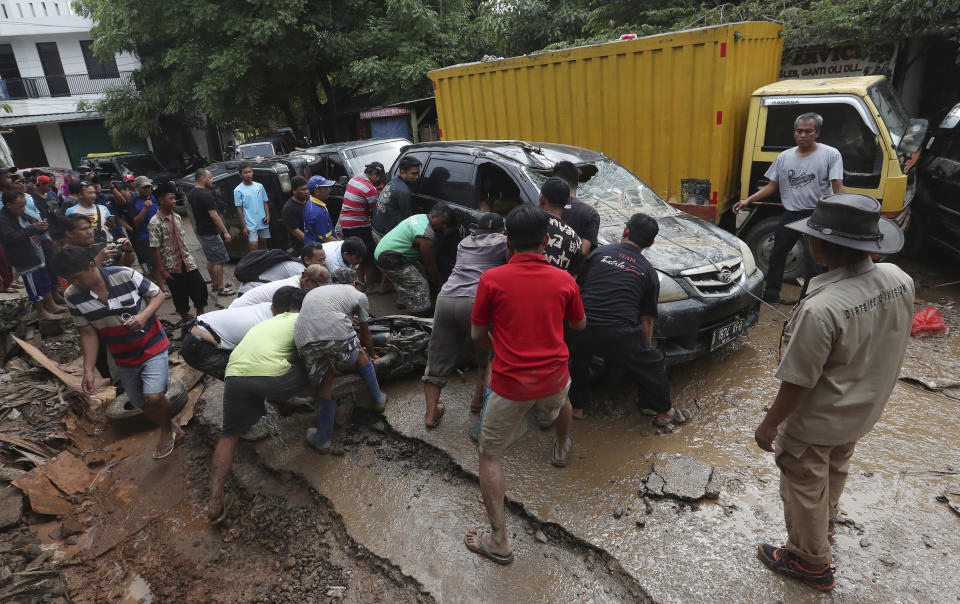 Residents try to move the wreckage of cars that were swept away by flood in Bekasi, West Java, Indonesia, Friday, Jan. 3, 2020.Severe flooding in greater Jakarta has killed scores of people and displaced tens of thousands others, the country's disaster management agency said. (AP Photo/Achmad Ibrahim)