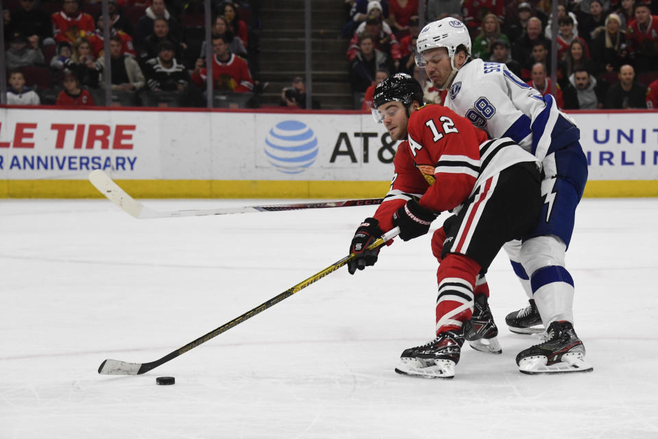 Chicago Blackhawks left wing Alex DeBrincat (12) and Tampa Bay Lightning defenseman Mikhail Sergachev (98) fight for the puck during the first period of an NHL hockey game, Sunday, March 6, 2022, in Chicago. (AP Photo/Matt Marton)