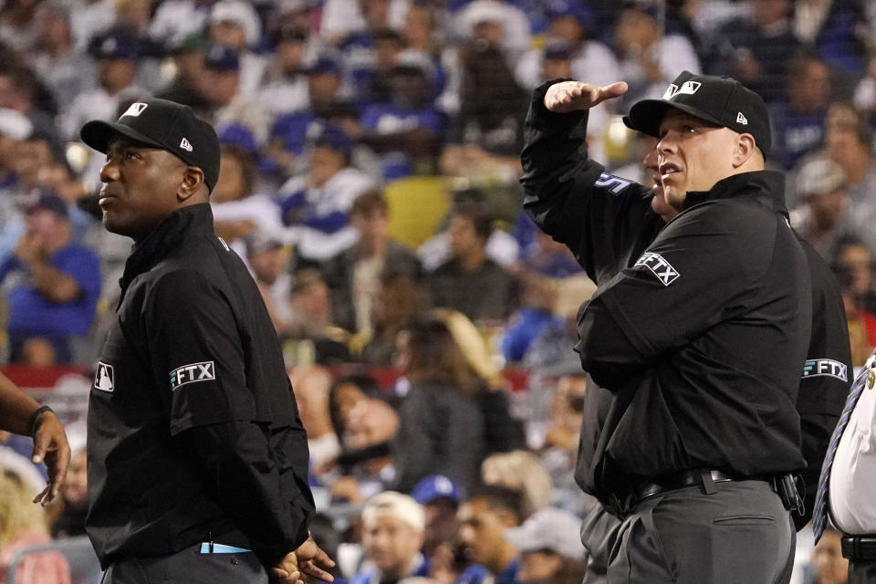 Umpires look toward the sky after a drone was seen above the field during the third inning of a baseball game between the Los Angeles Dodgers and the Colorado Rockies Tuesday, Oct. 4, 2022, in Los Angeles. The game was halted for several minutes due to the intrusion. (AP Photo/Mark J. Terrill)