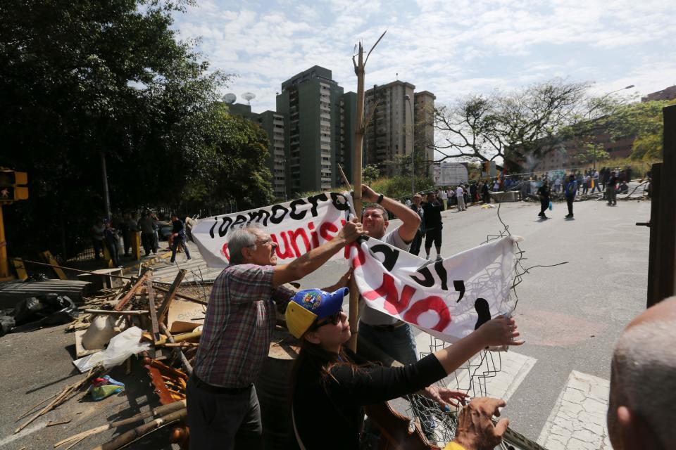 Demonstrators set up a banner that reads in Spanish "Democracy, Yes. Communism, No", as they set up a barricade in La Boyera neighborhood in Caracas, Venezuela, Thursday, Feb. 20, 2014. Violence is heating up in Venezuela as an opposition leader Leopoldo Lopez, faces criminal charges for organizing a rally that set off a deadly week of turmoil in anti-government protests in Caracas and other cities where demonstrators and government forces clashed leaving several dead and scores of wounded. (AP Photo/Fernando Llano)