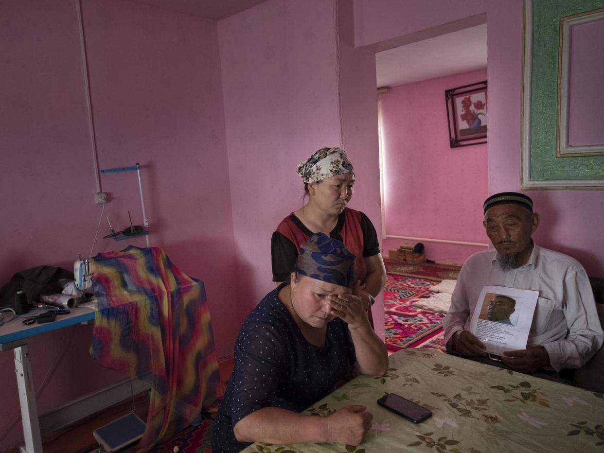 Auelkhan (centre) visits with Gulnar Kosdaulet (left), and Akbar Yenkelesh in their home in Akshi. Kosdaulet's husband, Sarsenbek Akbar, 45, is in a camp in Xinjiang. Yenkelesh, her father-in-law, holds up a photo of his son: Photo for The Washington Post by Joel van Houdt