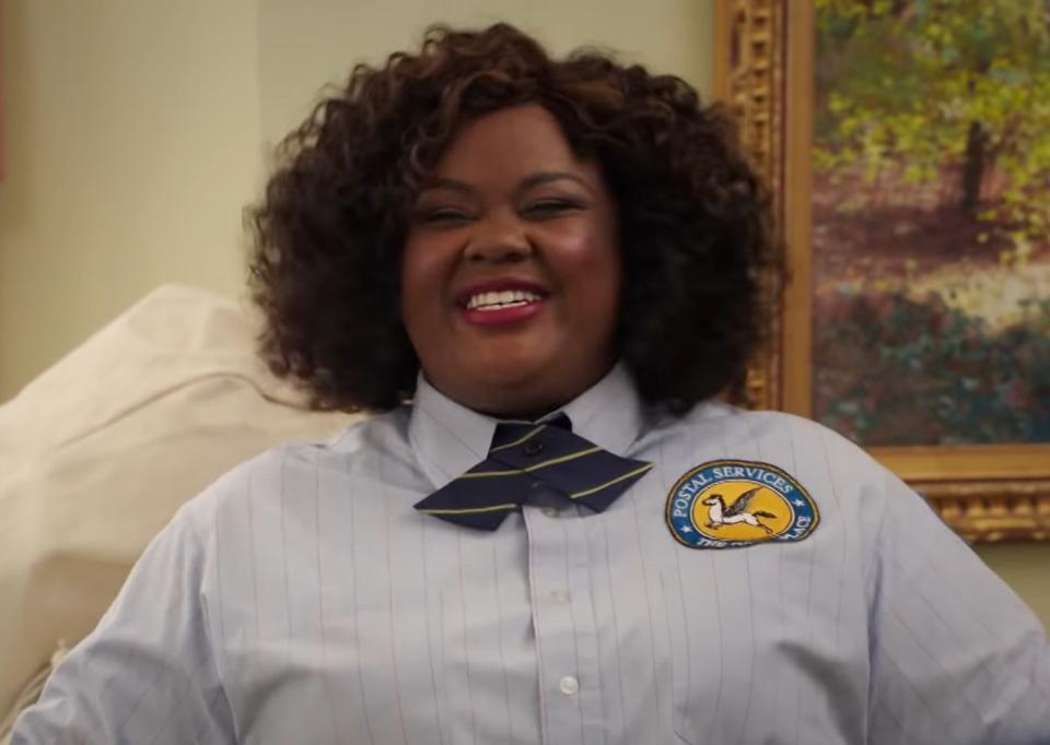 Nicole Byer as Gwendolyn, dressed as a postal worker and smiling