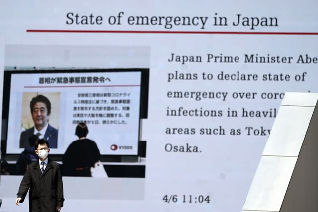 A man walks past a screen showing the news report that Japanese Prime Minister Shinzo Abe plans to declare a state of emergency over coronavirus in Tokyo