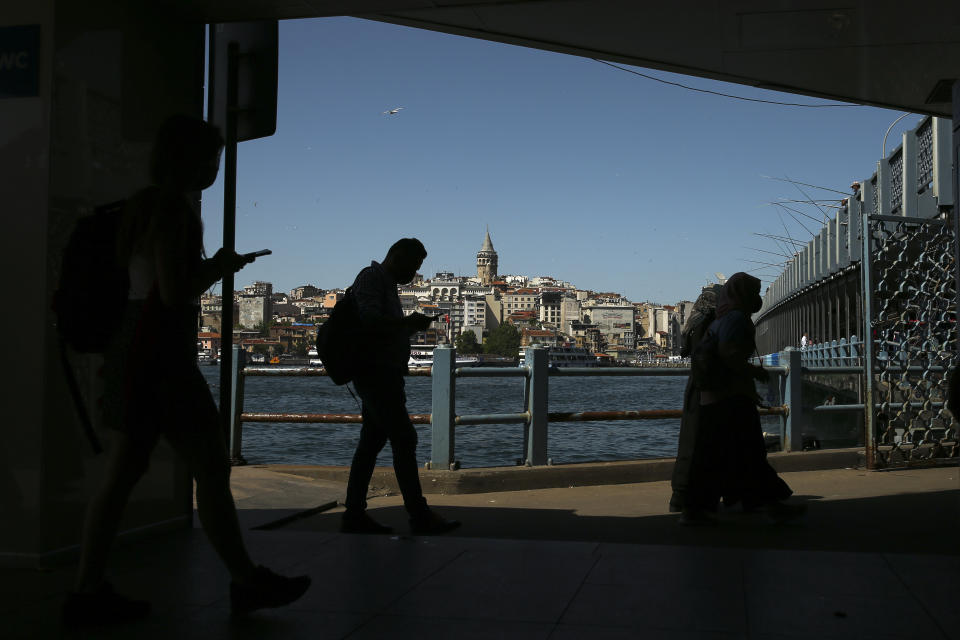 Backdropped by the iconic Galata Tower, people walk under the Galata Bridge over the Golden Horn leading to the Bosphorus Strait separating Europe and Asia, in Istanbul, Tuesday, May 25, 2021. (AP Photo/Emrah Gurel)