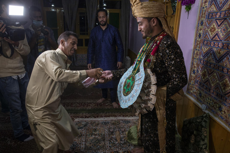 A Kashmiri man sprays sanitizer on the hand of Haseeb Mushtaq, a Kashmiri groom as he arrives at brides home during his wedding ceremony on the outskirts of Srinagar, Indian controlled Kashmir, Monday, Sept. 14, 2020. The coronavirus pandemic has changed the way people celebrate weddings in Kashmir. The traditional week-long feasting , elaborate rituals and huge gatherings have given way to muted ceremonies with a limited number of close relatives attending. With restrictions in place and many weddings cancelled, the traditional wedding chefs have little or no work. The virus has drastically impacted the life and businesses in the region. (AP Photo/ Dar Yasin)