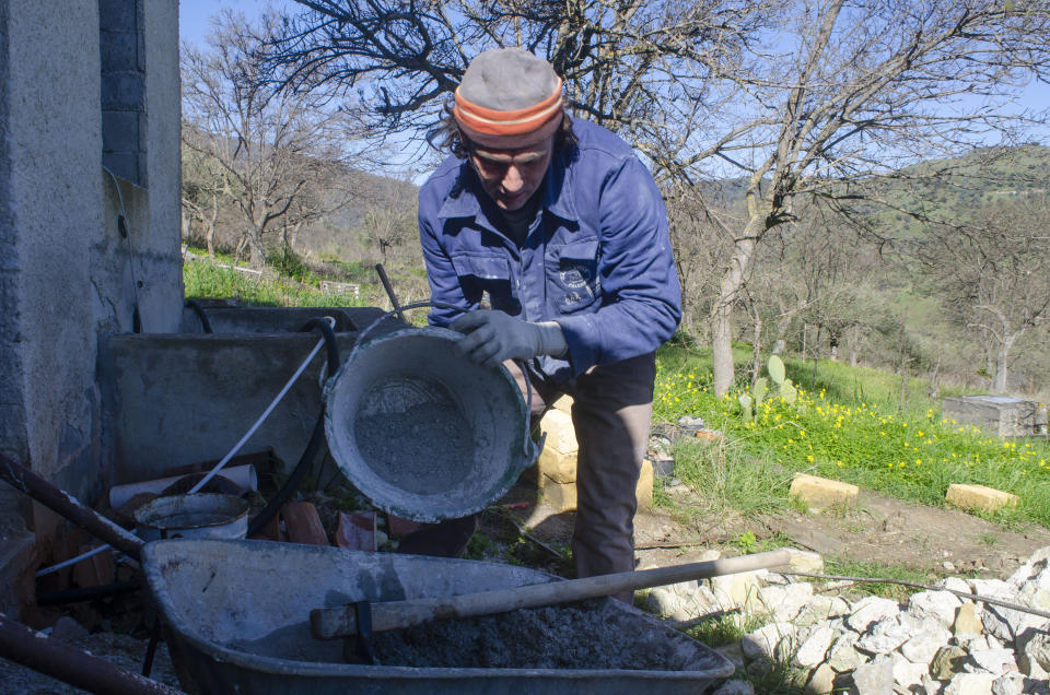 This image provided by Audrey Rodeman shows Cain Burdeau pouring water into a batch of concrete outside a concrete barn being renovated into a home in the countryside of Castelbuono, Sicily, Italy. Burdeau had to become familiar with masonry to build in Italy, a land where laborers have long excelled with trowels, chisels, mortar mixes, stones and bricks. (Audrey Rodeman via AP)