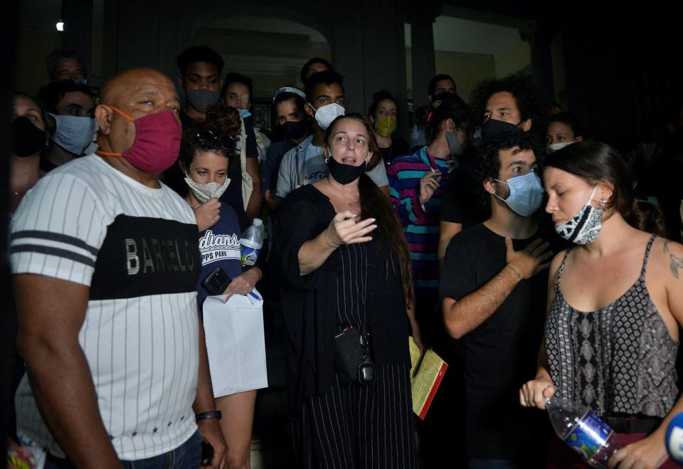 Woman in black wearing a facemask speaks, surrounded by a crowd