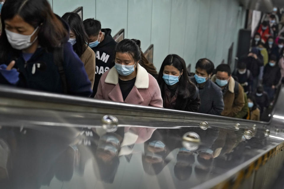 Commuters wearing face masks to help curb the spread of the coronavirus are reflected on a panels they ride an escalator at a subway station during the morning rush hour in Beijing, Tuesday, Nov. 17, 2020. (AP Photo/Andy Wong)